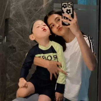 selfie, cermin, kakak adik, keluarga, pelukan, ekspresi lucu, wajah manyun, wajah cemberut, pakaian renang anak, topi renang, kaos putih, wanita, anak laki-laki, ponsel, casing ponsel bunga, momen kebersamaan, kedekatan, kebahagiaan, keakraban, kamar mandi, dinding marmer, potret diri, cinta keluarga, bermain, kecerian, gaya santai, pakaian olahraga, interaksi, momen indah, kenangan