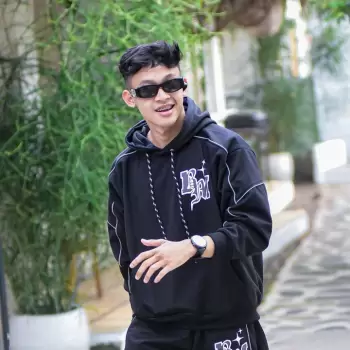 pria, muda, gaya, kasual, hoodie, hitam, celana pendek, kacamata hitam, trendi, modern, santai, pose, tersenyum, rambut hitam, percaya diri, luar ruangan, jalan, latar belakang hijau, daun, vegetasi, cerah, siang hari, streetwear, fashion, anak laki-laki, wajah, ekspresi, tampilan, anak muda, pria bergaya