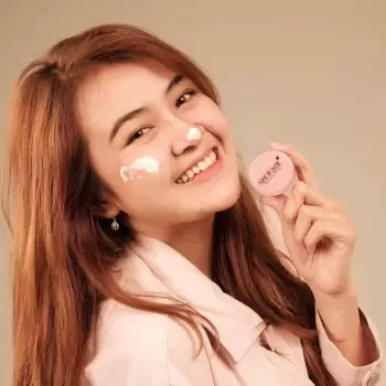 wanita, muda, tersenyum, bahagia, produk kecantikan, krim wajah, kulit bersih, perawatan kulit, perawatan wajah, kosmetik, tabir surya, melembabkan, mencerahkan, kemasan produk, wadah bulat, logo, label, brand, iklan, promosi, gaya hidup, sehat, cantik, makeup, model, studio, latar belakang polos, warna kulit, tekstur kulit