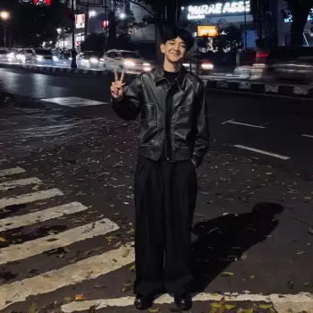 pria muda, fashion pria, jaket kulit, celana longgar, jalanan malam, kota, lampu jalan, lalu lintas, zebra cross, trotoar, daun kering, gaya santai, pose v, tersenyum, ekspresi ceria, anak muda, urban, bergaya, kasual, mode jalanan, suasana malam, pencahayaan kota, bebas, percaya diri, berdiri, di luar ruangan, kontras, bayangan, siluet, pemandangan kota.