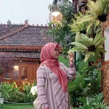wanita, muslim, hijab, pakaian, atasan, rok, motif garis, tas, keranjang, hijau, tanaman, daun, bunga, alam, luar ruangan, bangunan, rumah, tradisional, atap genteng, lampu, hiasan, dekorasi, suasana, tenang, santai, cerah, siang, sore, pemandangan, alam pedesaan